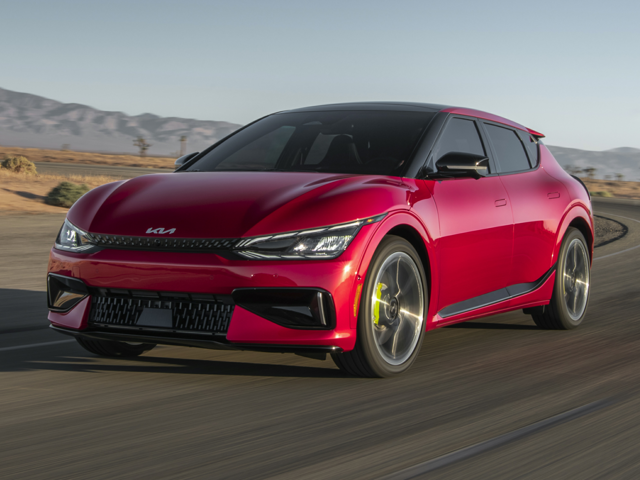 A red 2025 Kia EV6 speeding on a road with mountains in the background.