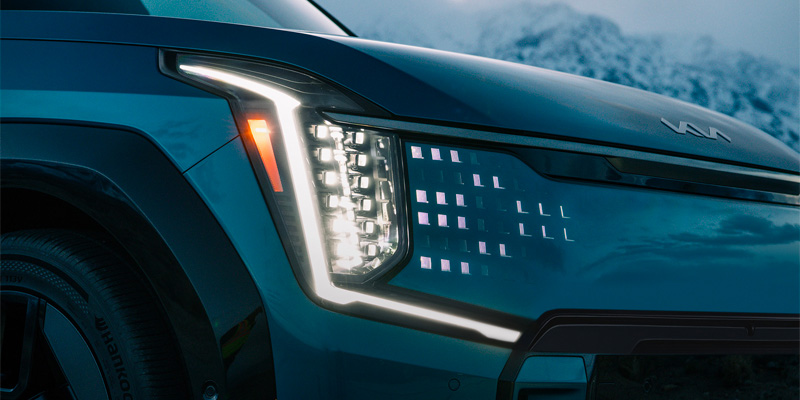 Close-up of a modern 2025 Kia EV9 SUV's front headlight with LED lights and sleek design.